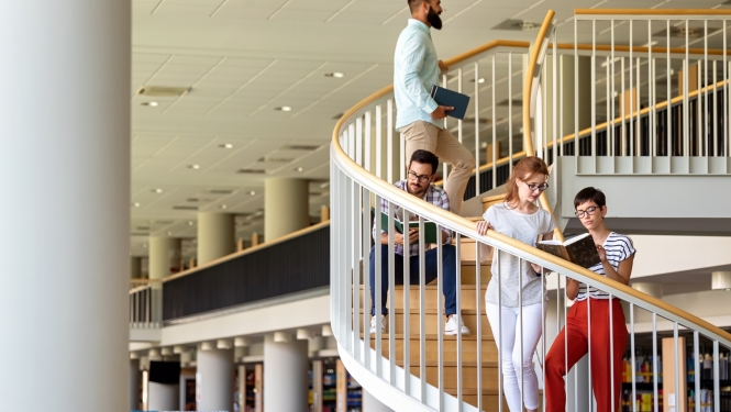 Studenti augstskolā. Fonā grāmatu plaukti. 