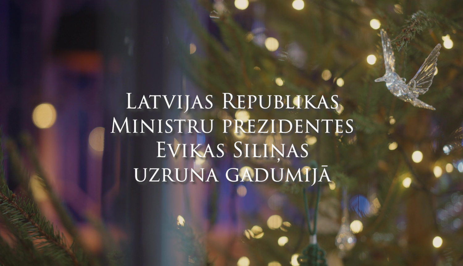 Uzraksts Latvijas Republikas Ministru prezidentes Evikas Siliņas uzruna gadumijā, fonā attēls ar gaismiņām eglītes zaros