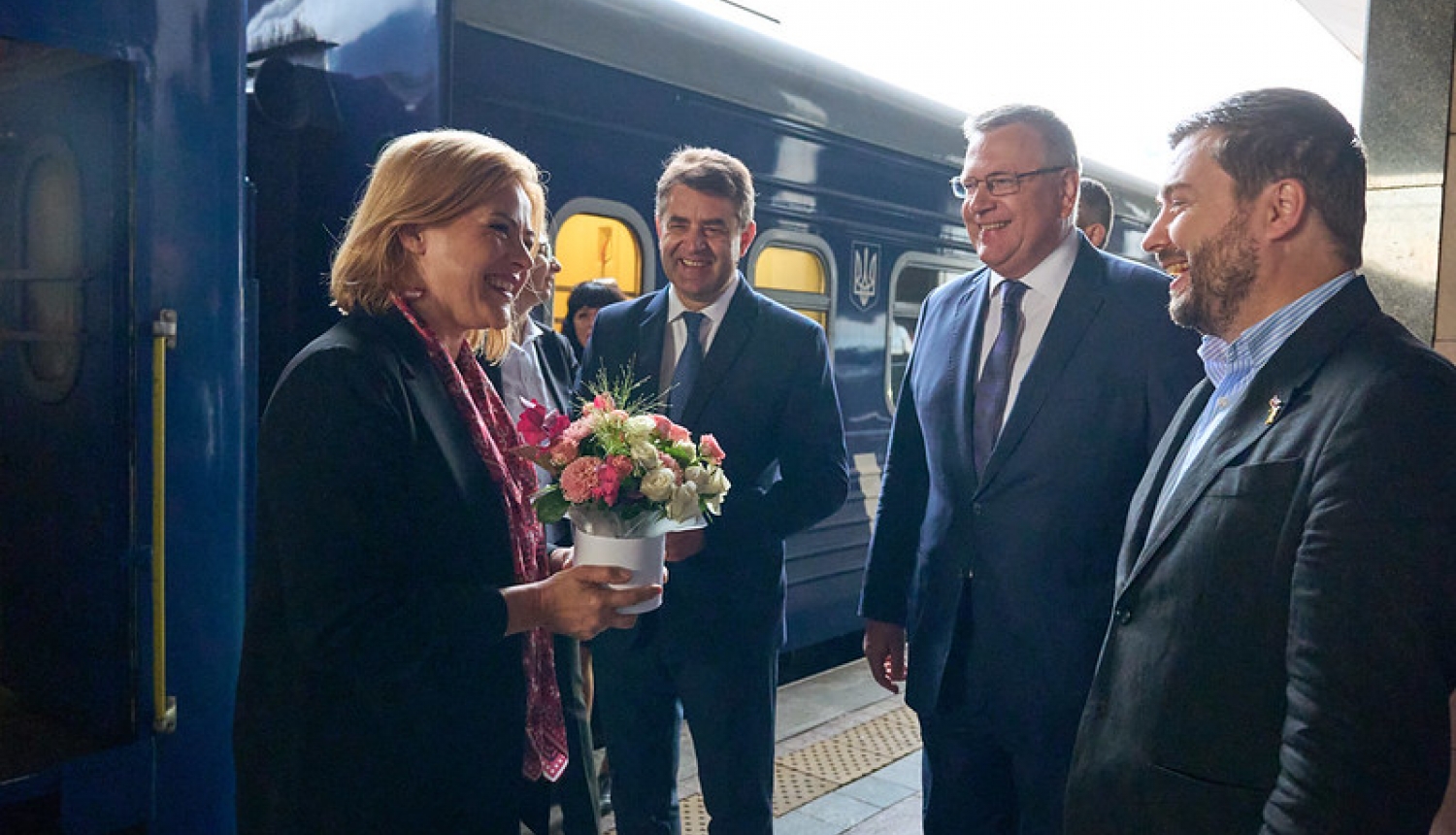 Ministru prezidente Evika Siliņa Kijivā. Ministru prezidenti sagaida amatpersonas.  Fonā vilciens. 